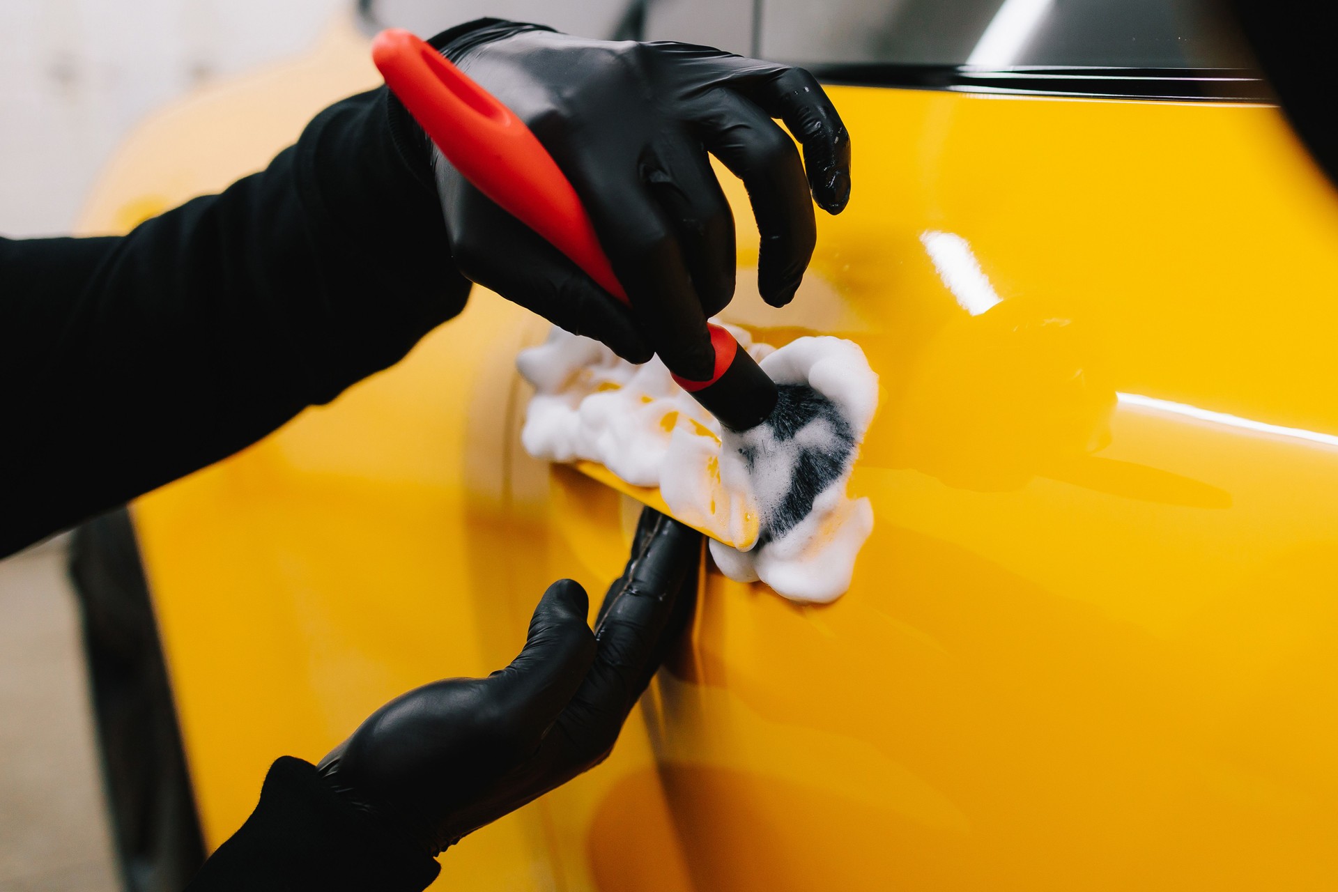 Car washer is brushing car handle body after washing automobile. Car handle washing with microfiber and detergent in detailing auto service.