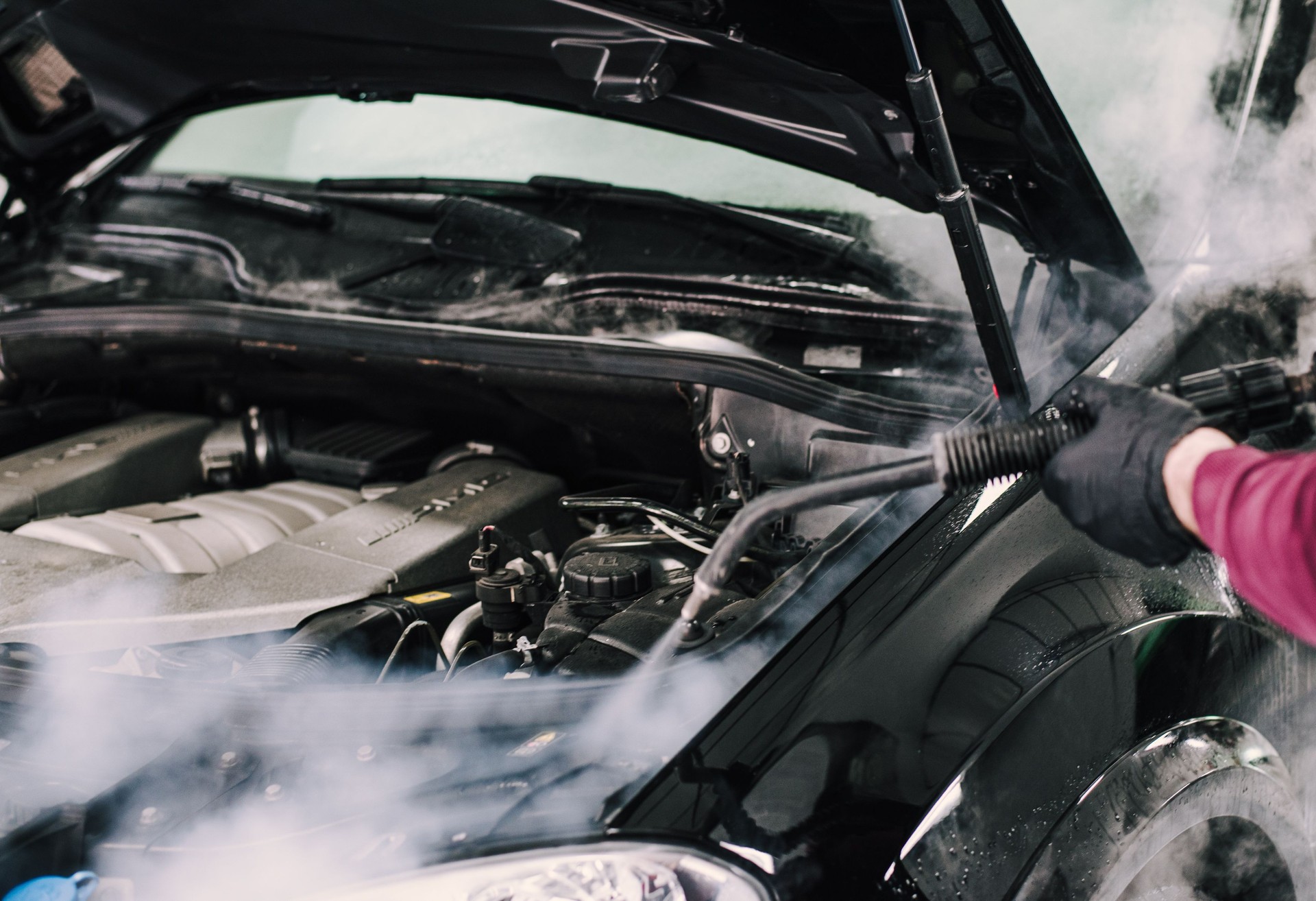 Man using steam to clean a car hood